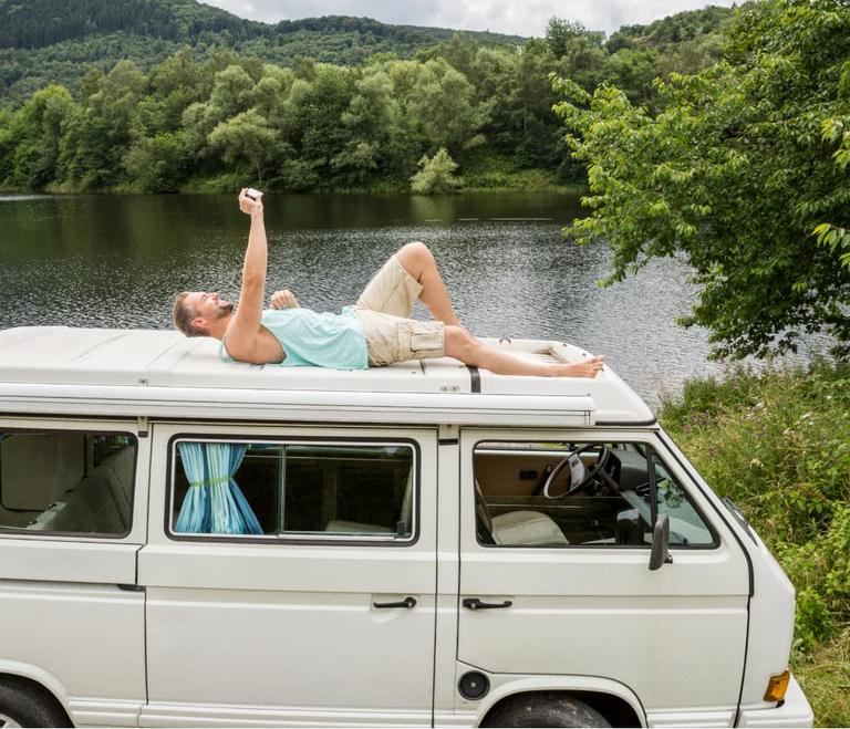 Man on the roof of a van with looking his phone